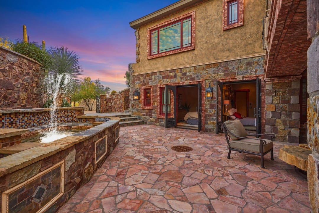 Stone patio with fountain and chairs.