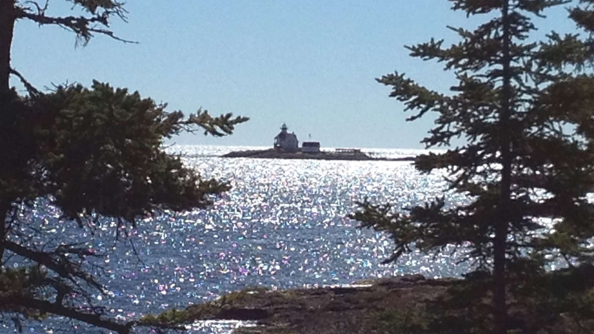 Lighthouse across sparkling ocean water.