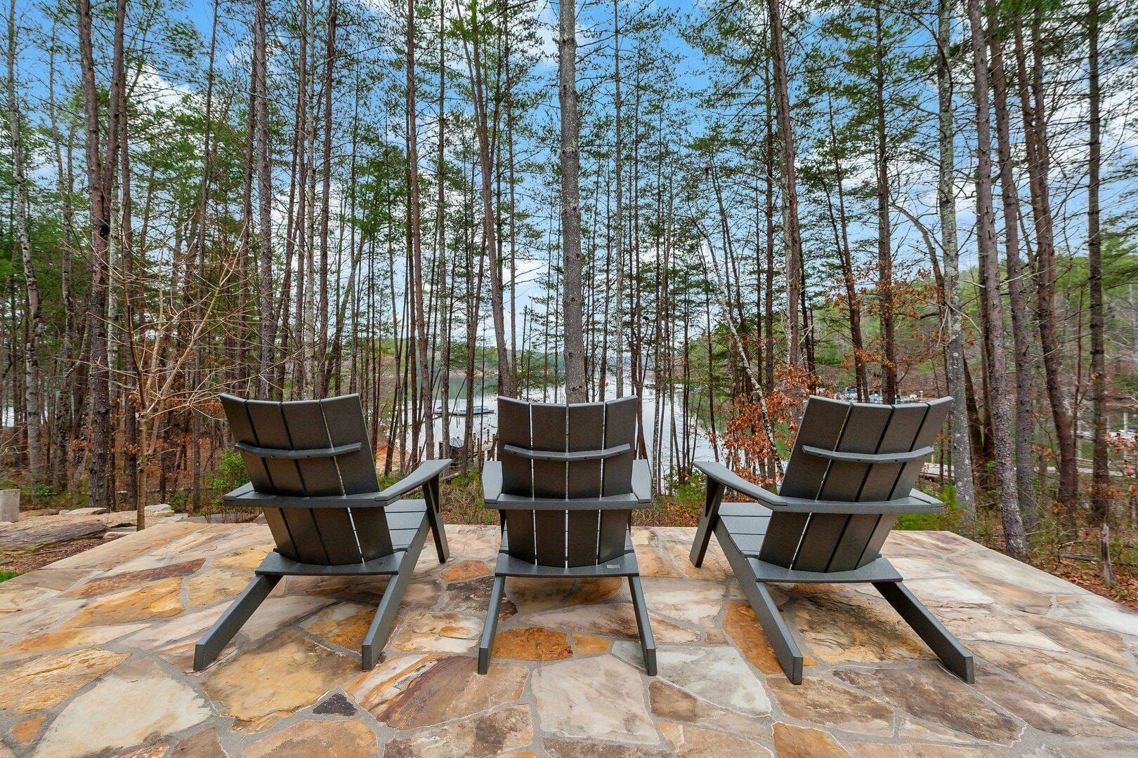 Three chairs facing wooded lake.