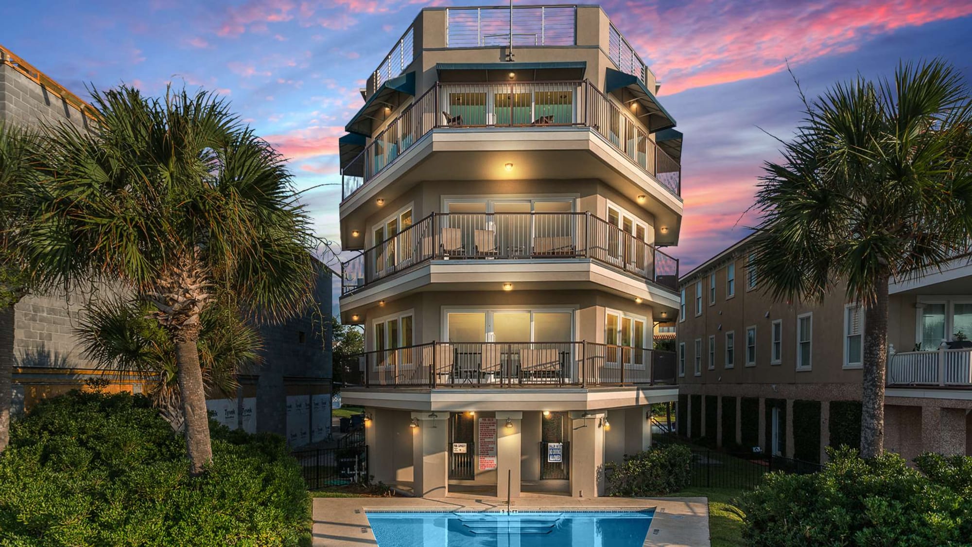 Four-story building with pool, sunset.