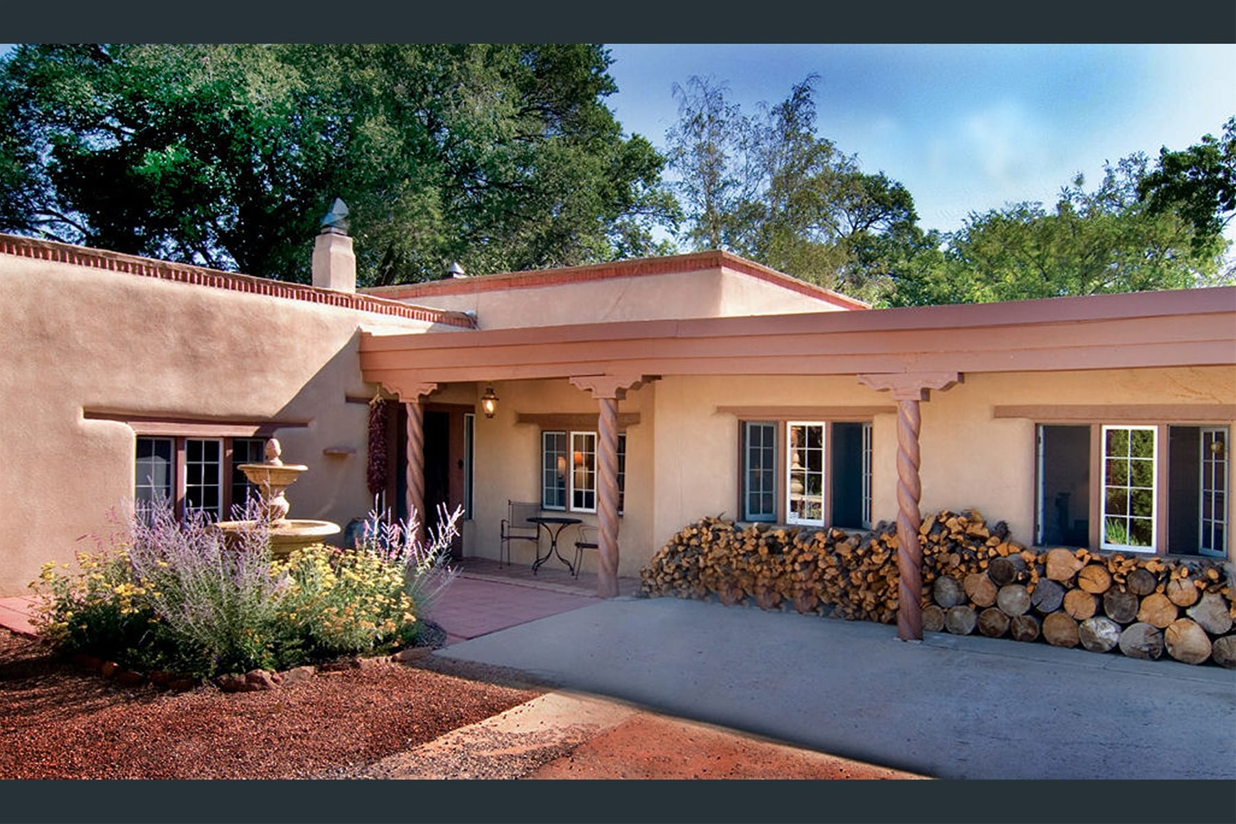 Adobe house with woodpile and plants.