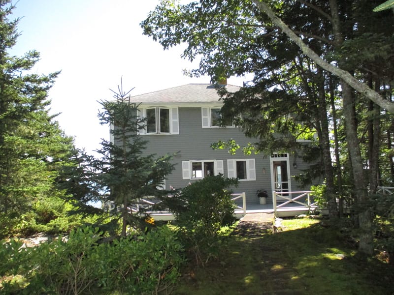 Grey house surrounded by trees.