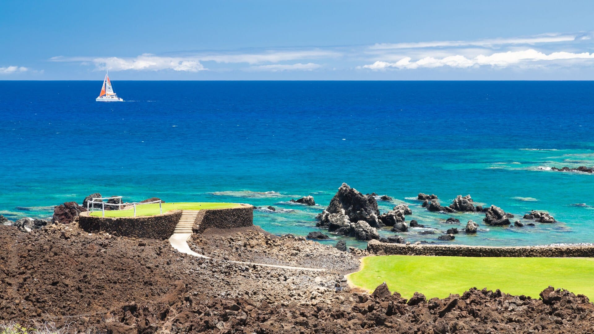 Sailboat on blue ocean near coastline.