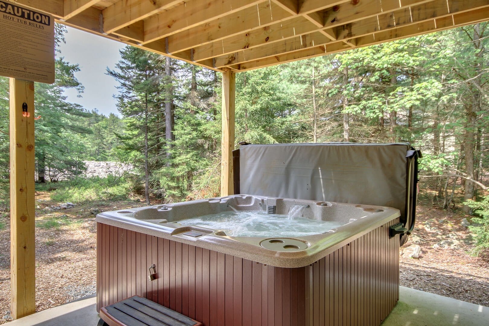 Hot tub under wooden canopy, forest.