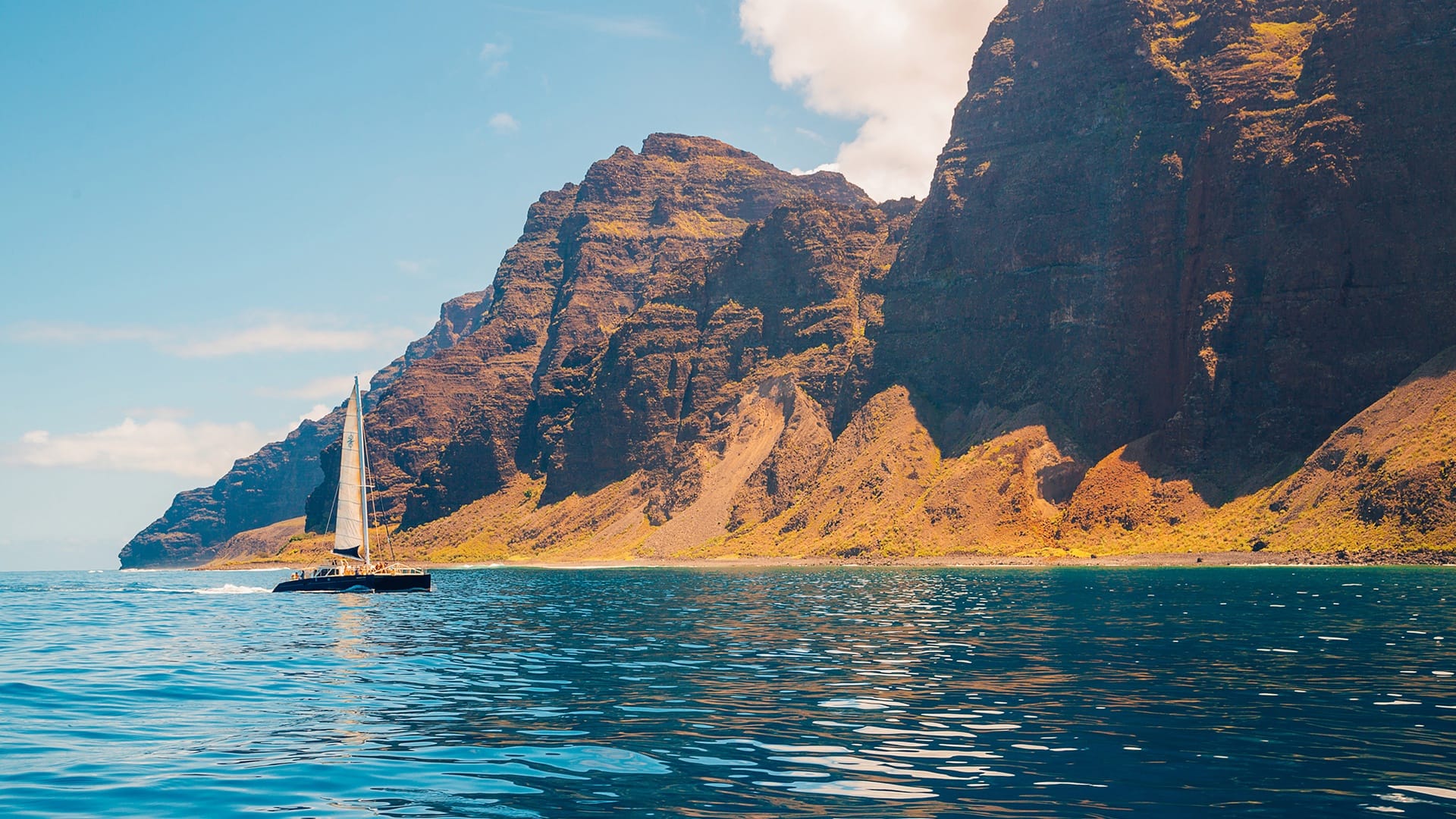 Sailboat near rugged coastal cliffs.