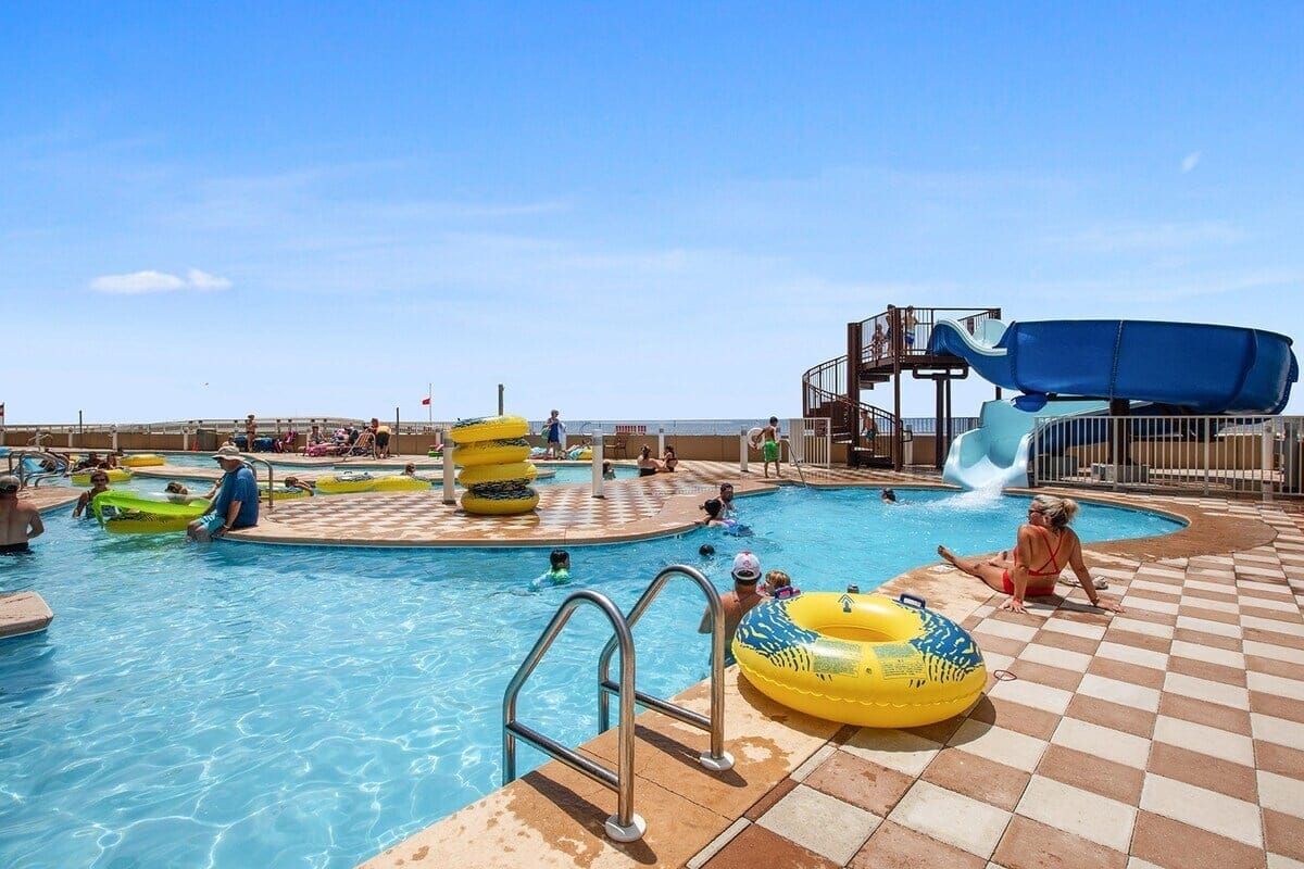 Outdoor pool with waterslide and people.