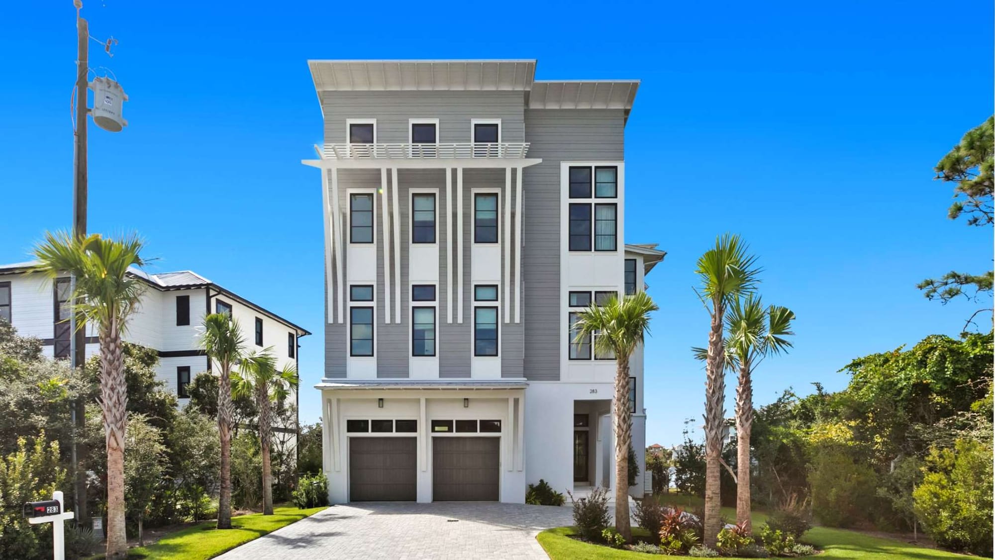 Modern three-story house with palm trees.