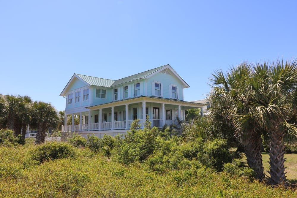 Light blue house, palm trees, bushes.