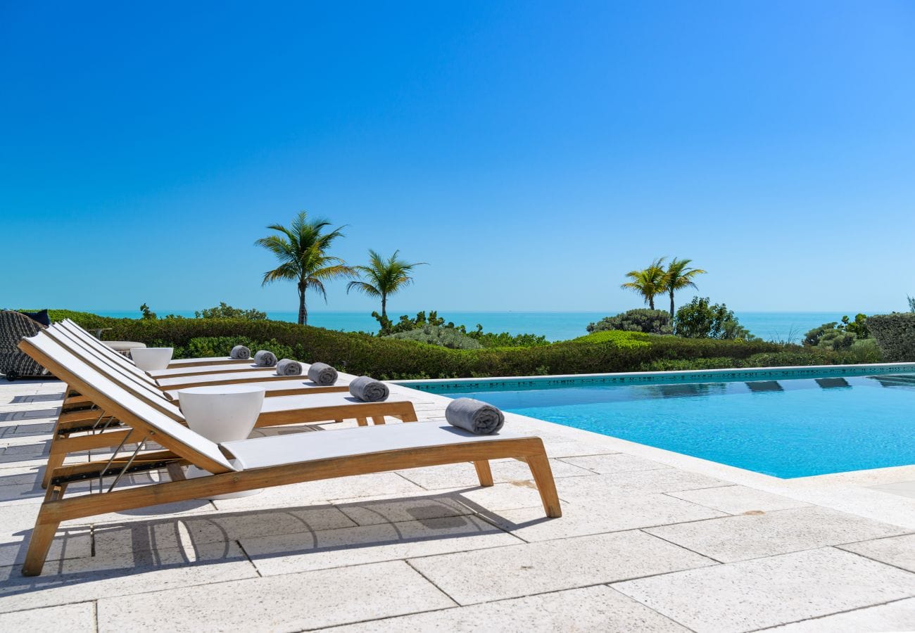 Poolside loungers, ocean view, palm trees.