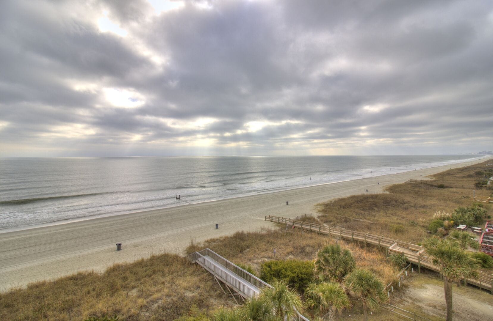 Cloudy beach with boardwalk and ocean.