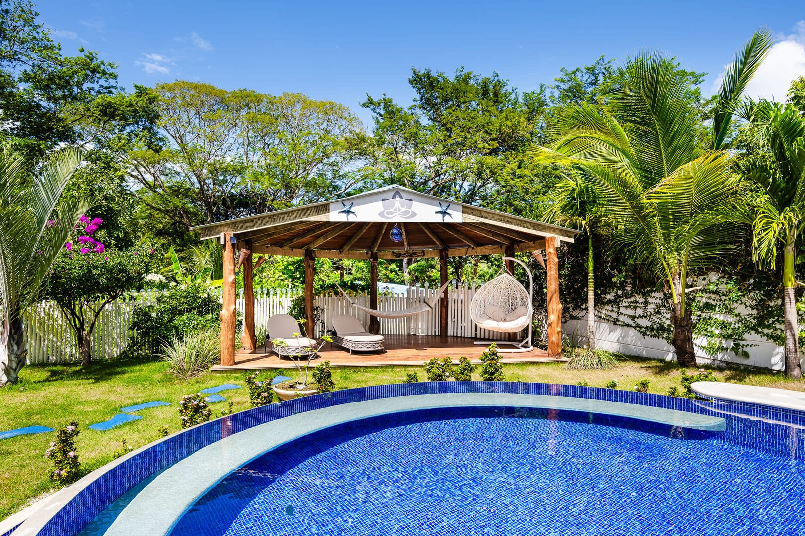 Poolside gazebo with hammock, greenery.