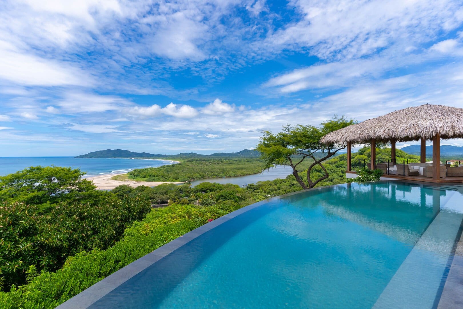 Infinity pool overlooking beach and trees.