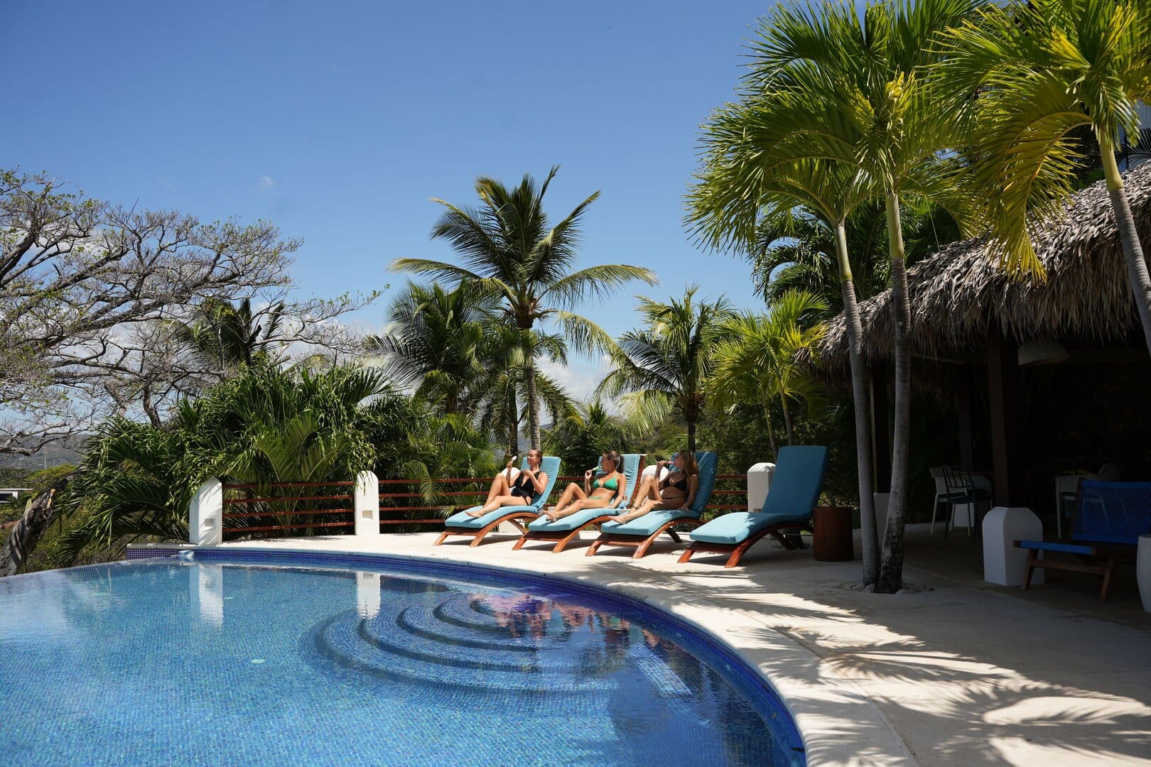 People relaxing by pool, palm trees.
