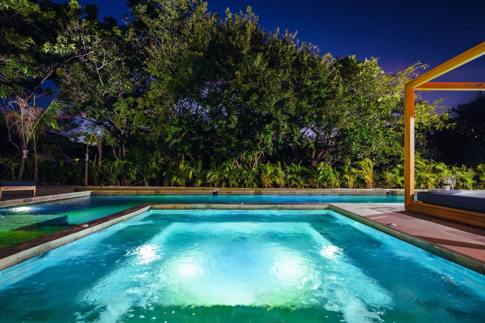 Illuminated pool at night, surrounded trees.
