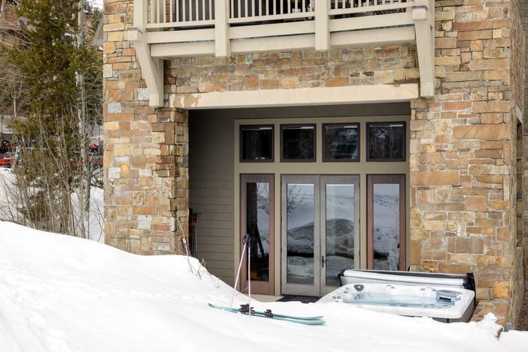 Snowy patio with skis and hot tub.