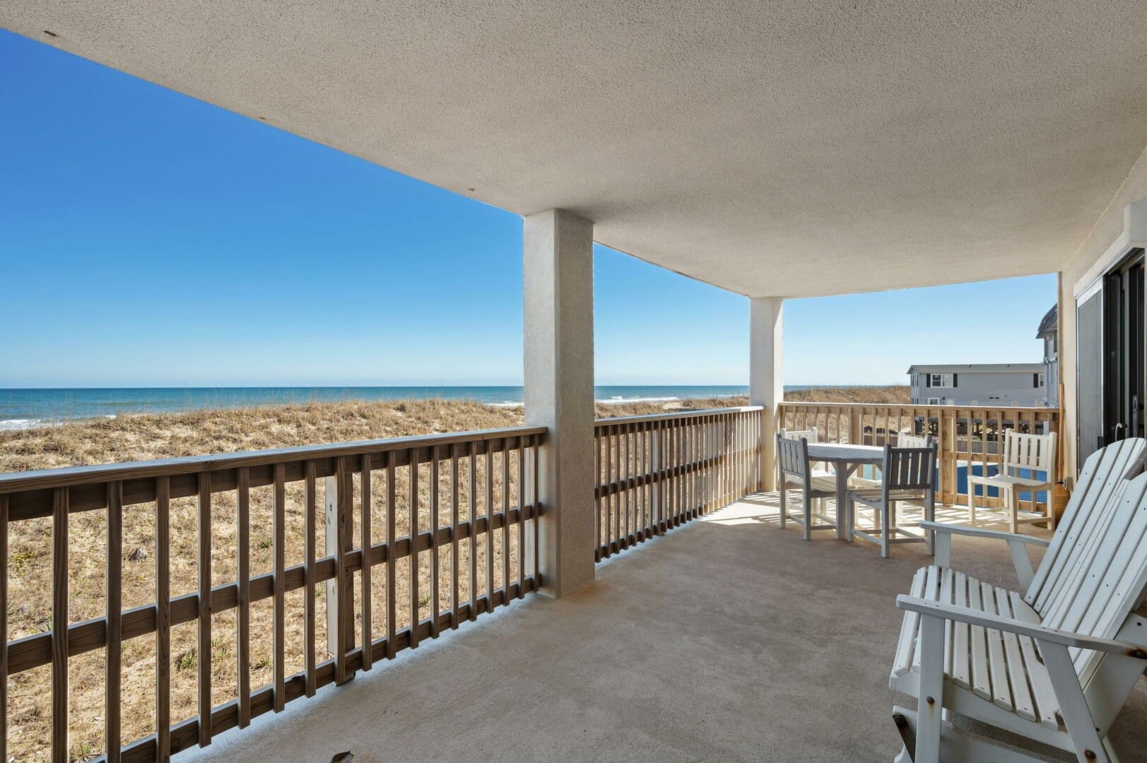 Beachfront balcony with chairs, table.