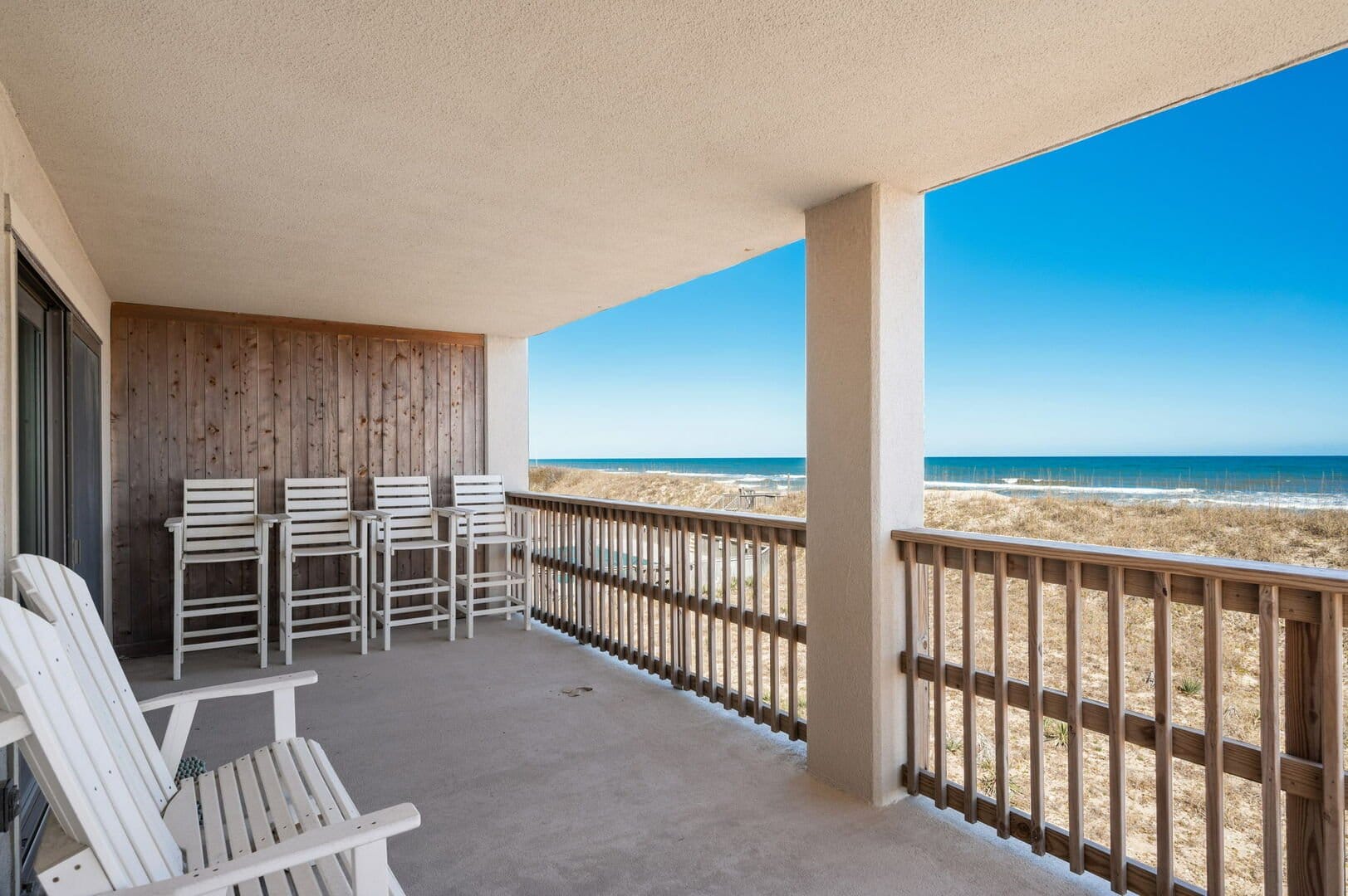 Beachfront balcony with white chairs.