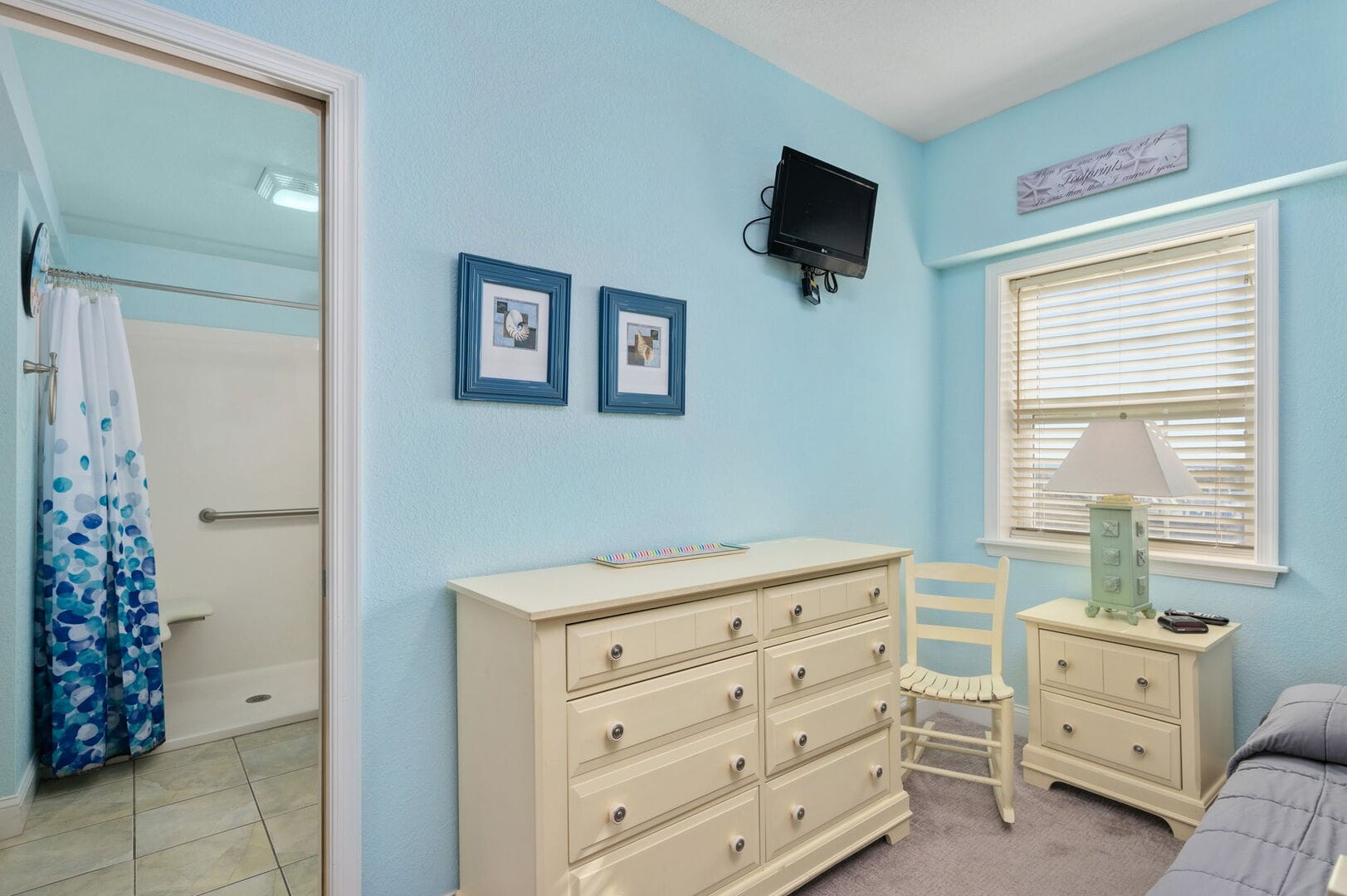 Blue bedroom with dresser and TV.